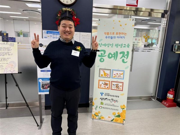 장애성인 평생교육 공예전 배너 옆에서 웃으며 서있는 참여자의 사진