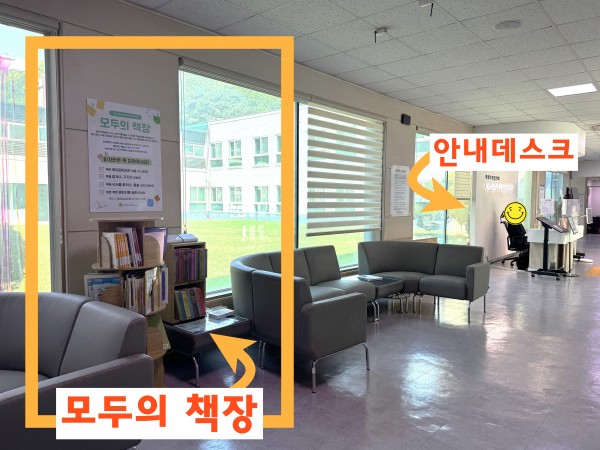 복지관 1층 현관 로비에 안네데스크와 소파가 있는 모습 그 옆에 모두의 책장이 마련되어있다