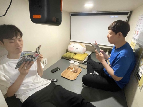 두명의 참여자가 신발을 벗고 편하게 앉아서 만화책을 보고 있습니다.