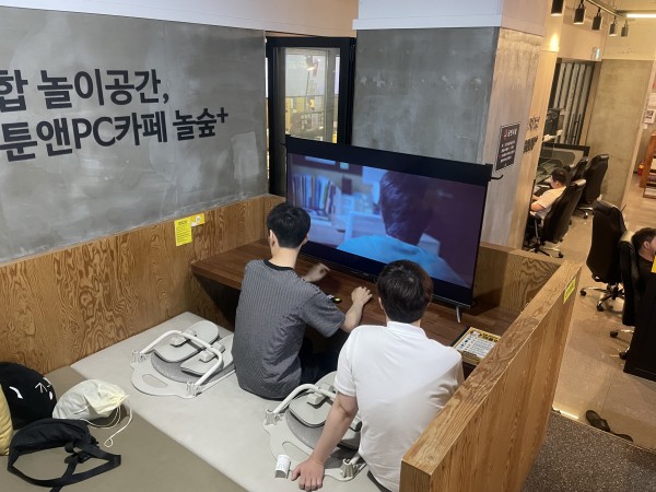 동아리원 2명이 매트 위에 앉아서 커다란 티비화면으로 영화를 보고 있습니다.