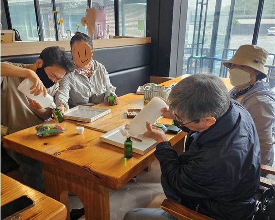 4명의 사람이 하얀색병에 든 액채(천연모기퇴치제 재료)를 초록색 병에 넣고 있다. 모두 마스크를 했고 한 사람은 얼굴을 가렸다.